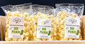 Three bags of Dill Pickle Protein Popcorn in a cardboard box with a dark background