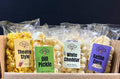 Assorted popcorn packages in a cardboard box with visible labels on a dark background