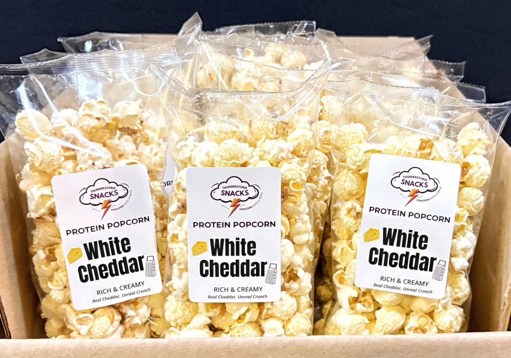 Box of protein popcorn labeled 'White Cheddar' with clear packaging.